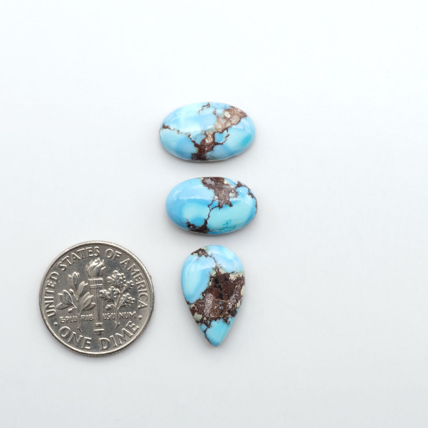 Golden Hills Turquoise cabochons, icy blue to lavender tones with chocolate matrix, polished stones on a white background with a US dime for scale