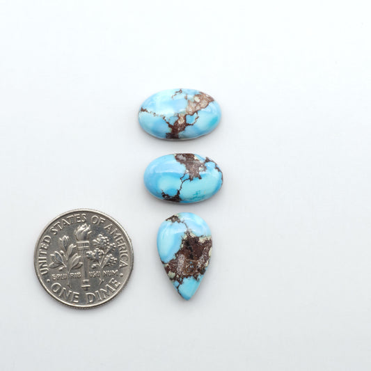 Golden Hills Turquoise cabochons, icy blue to lavender tones with chocolate matrix, polished stones on a white background with a US dime for scale