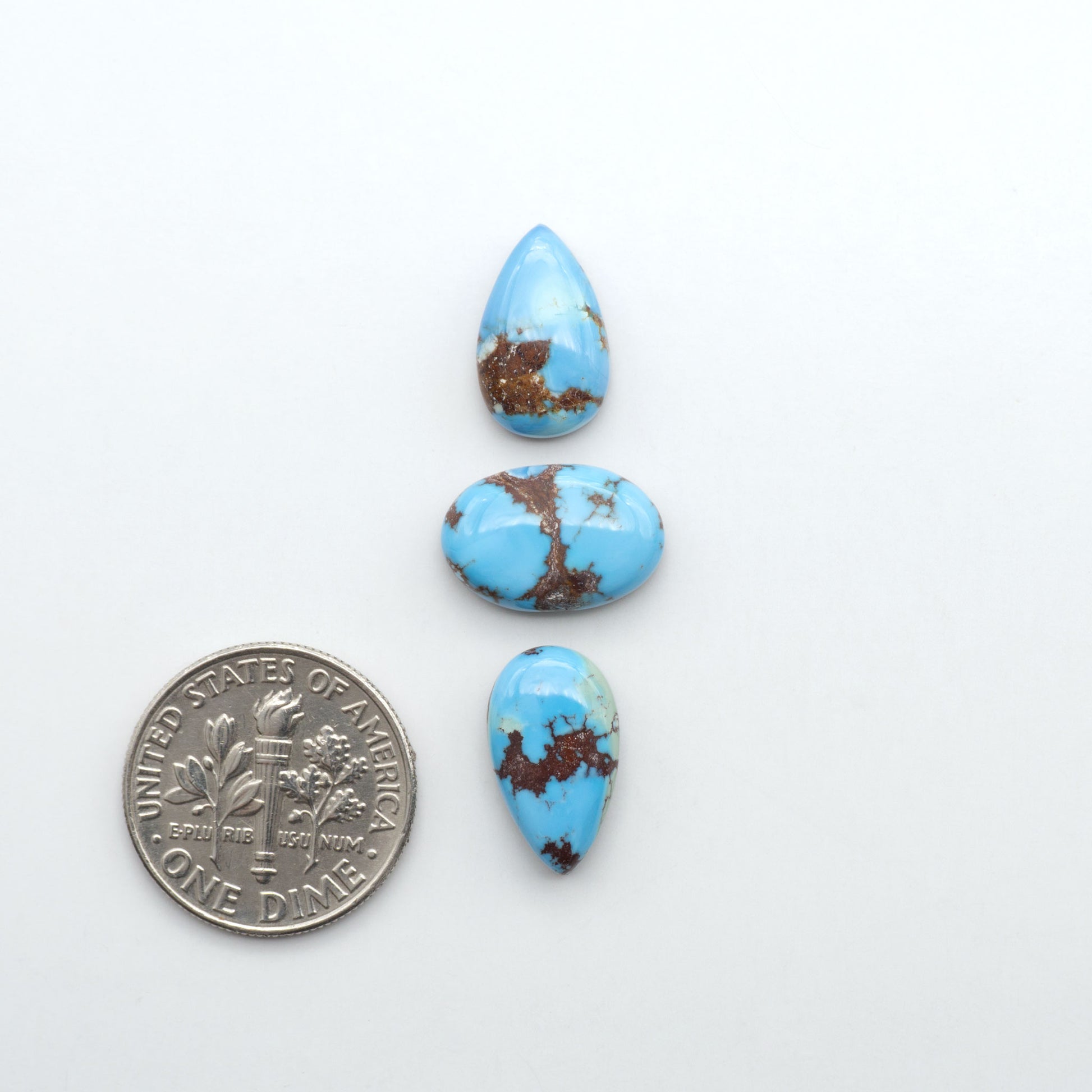 Golden Hills Turquoise cabochons, icy blue to lavender tones with chocolate matrix, polished stones on a white background with a US dime for scale