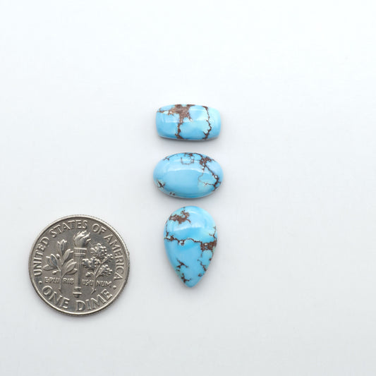 Golden Hills Turquoise cabochons, icy blue to lavender tones with chocolate matrix, polished stones on a white background with a US dime for scale