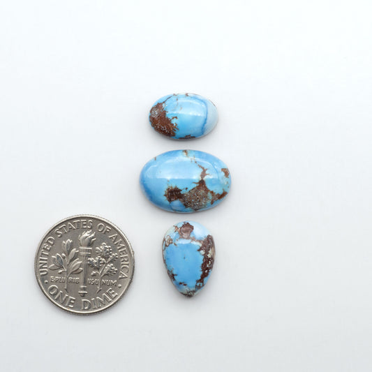 Golden Hills Turquoise cabochons, icy blue to lavender tones with chocolate matrix, polished stones on a white background with a US dime for scale