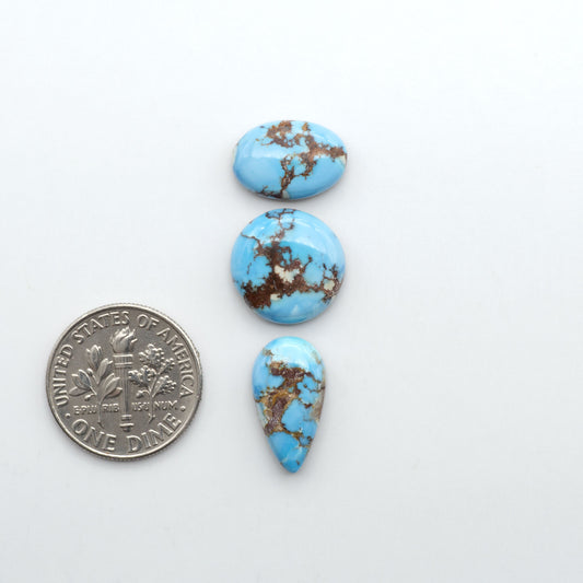 Golden Hills Turquoise cabochons, icy blue to lavender tones with chocolate matrix, polished stones on a white background with a US dime for scale