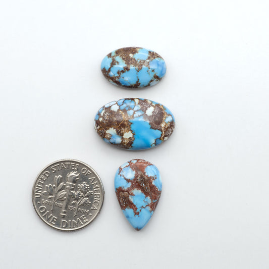 Golden Hills Turquoise cabochons, icy blue to lavender tones with chocolate matrix, polished stones on a white background with a US dime for scale