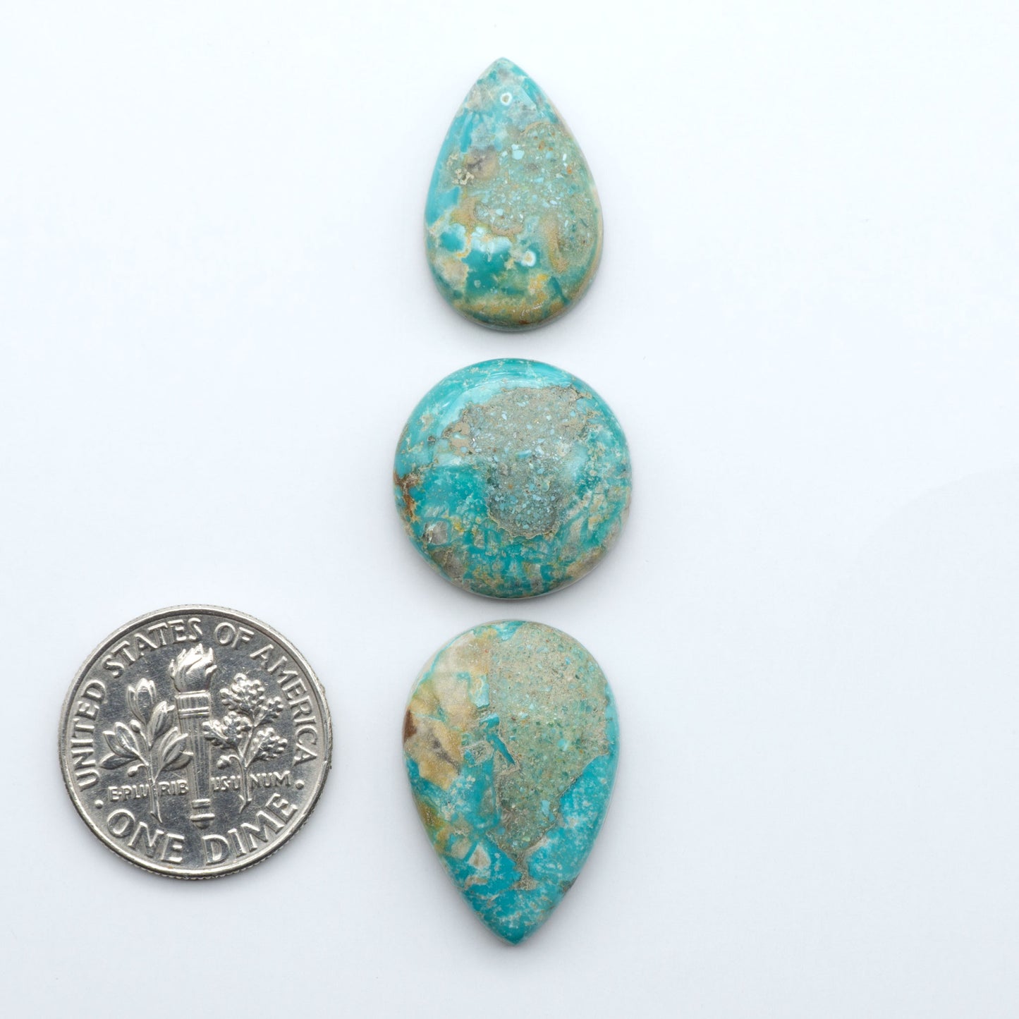 Fox Turquoise cabochons, polished gemstones with natural matrix on a white background, with a US dime for scale