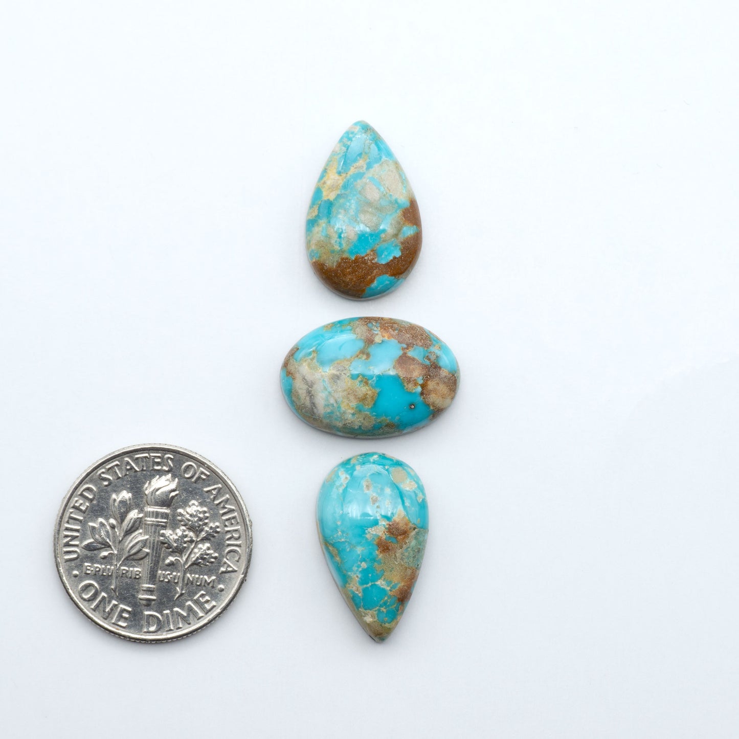 Fox Turquoise cabochons, polished gemstones with natural matrix on a white background, with a US dime for scale