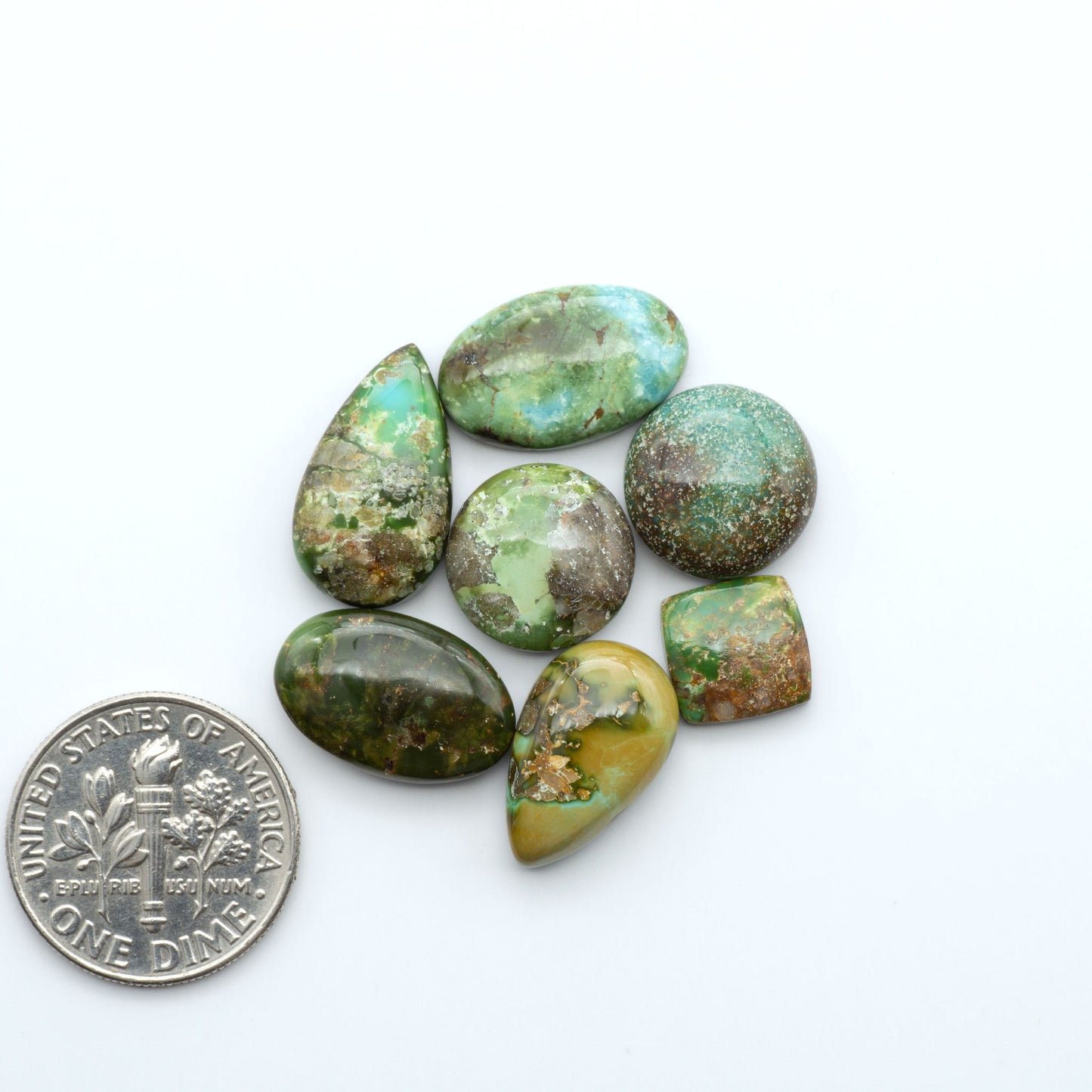 Sonoran Mountain Turquoise cabochons, blue-green color with natural matrix, polished stones on a white background, with a US dime for scale