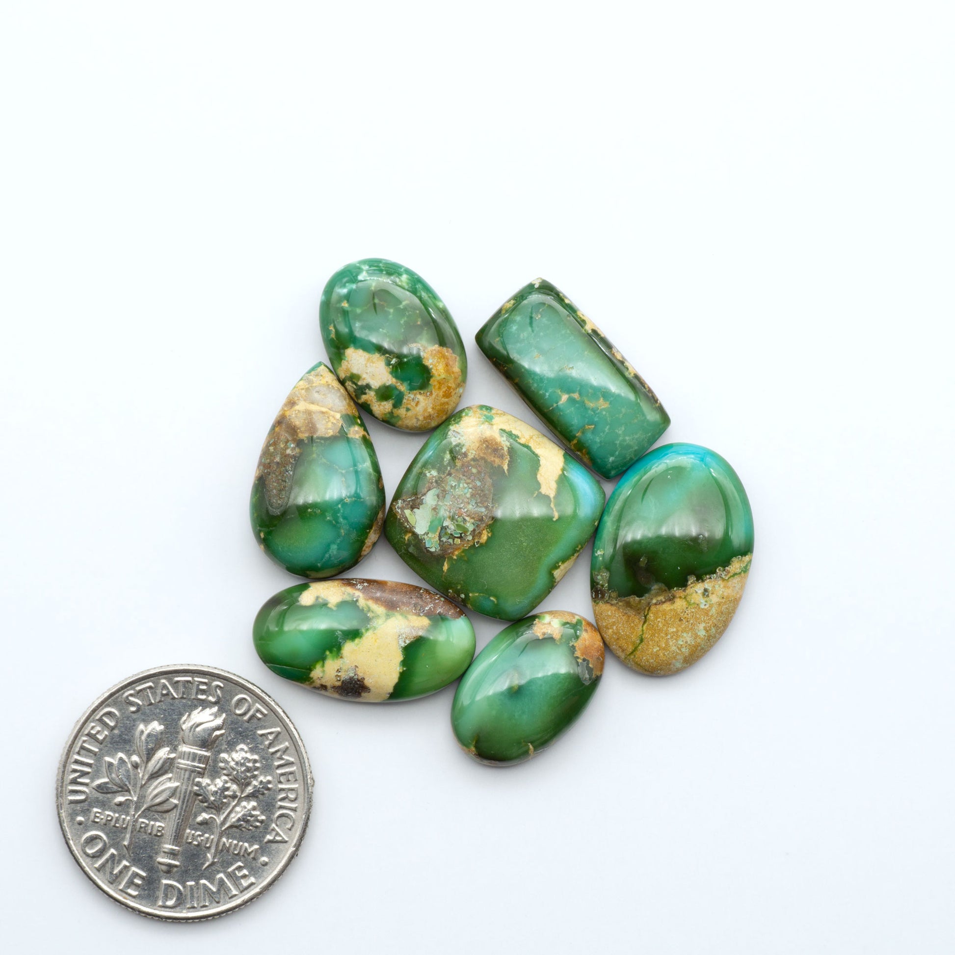 Sonoran Mountain Turquoise cabochons, blue-green color with natural matrix, polished stones on a white background, with a US dime for scale