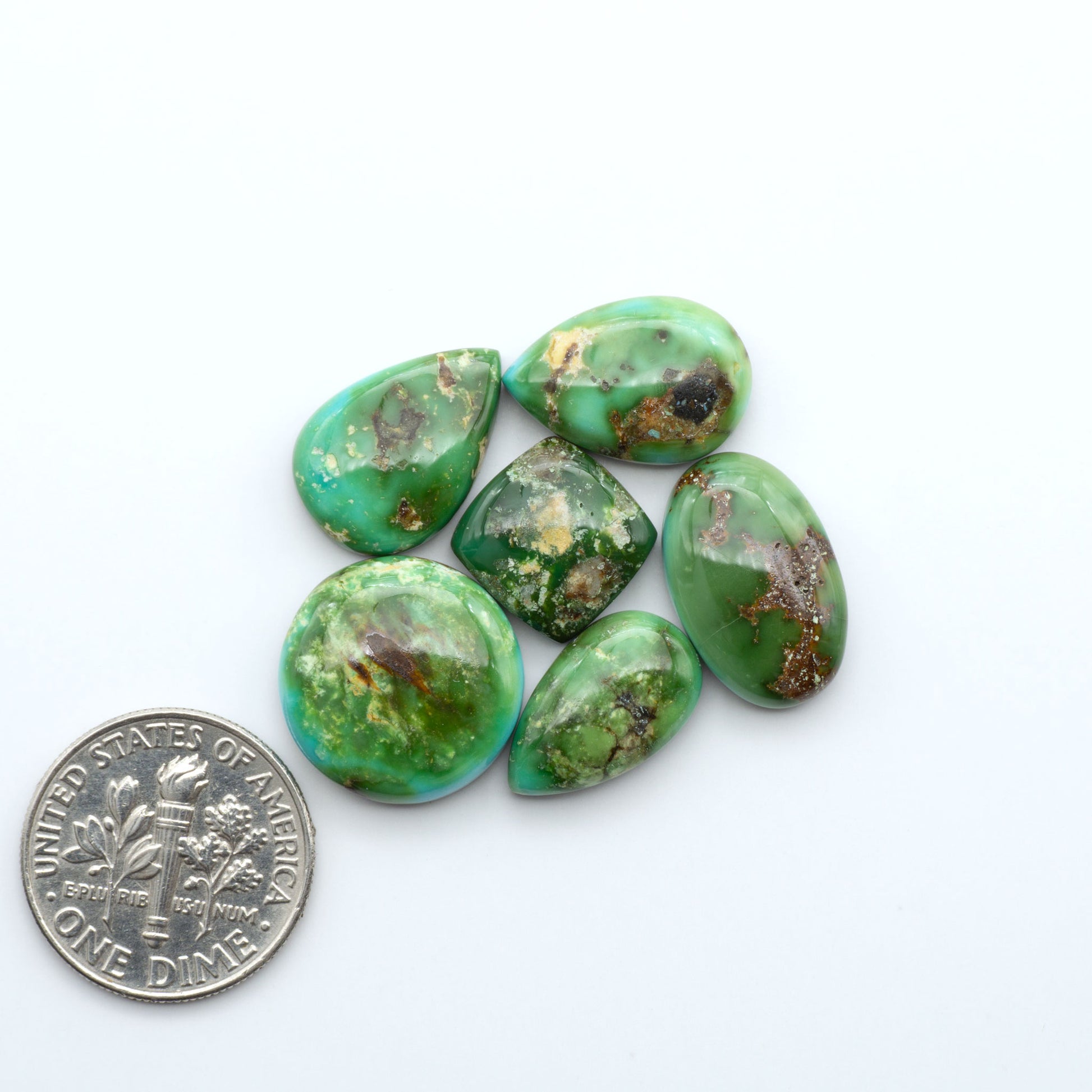 Sonoran Mountain Turquoise cabochons, blue-green color with natural matrix, polished stones on a white background, with a US dime for scale
