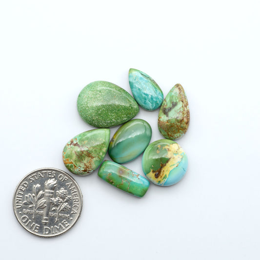 Sonoran Mountain Turquoise cabochons, blue-green color with natural matrix, polished stones on a white background, with a US dime for scale