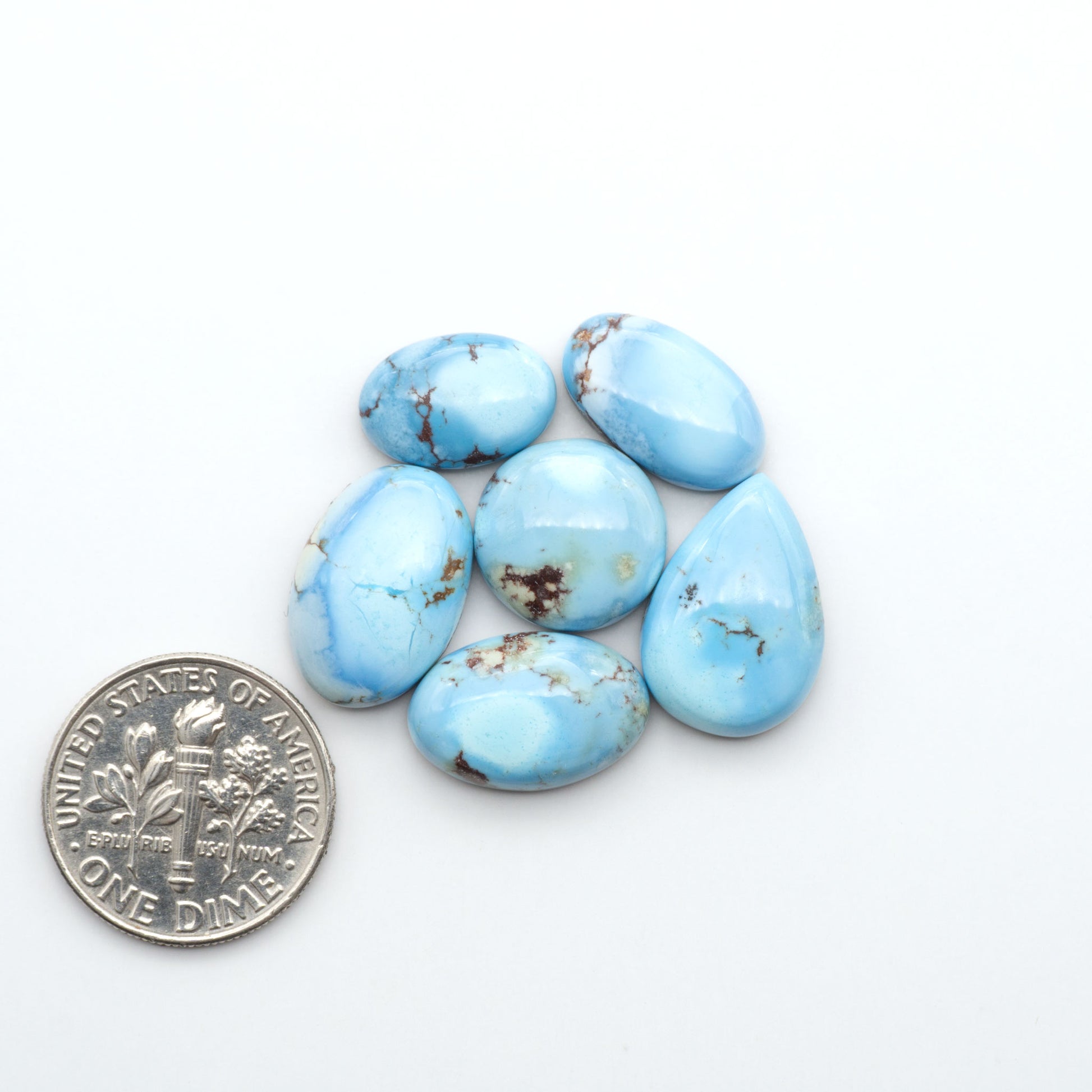 Golden Hills Turquoise cabochons, icy blue to lavender tones with chocolate matrix, polished stones on a white background with a US dime for scale