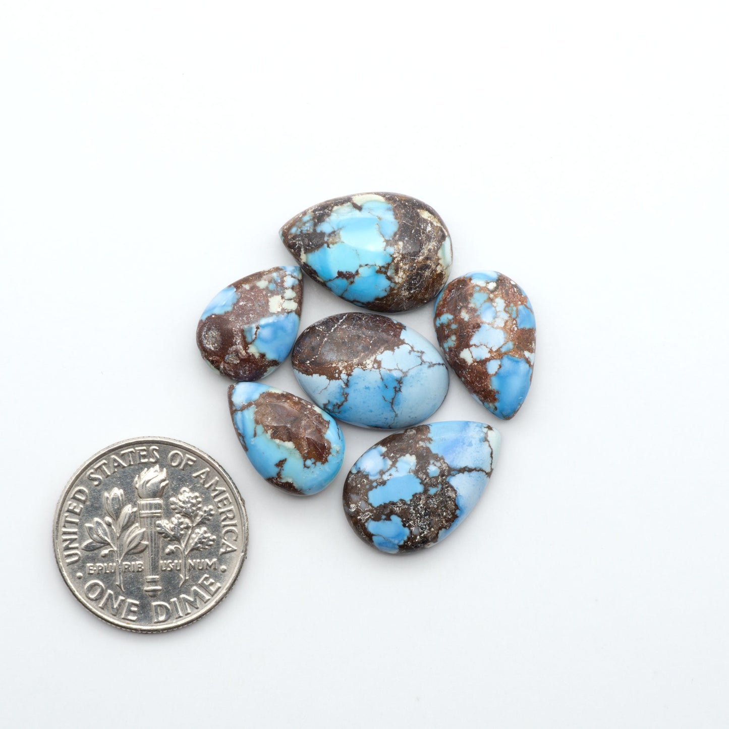 Golden Hills Turquoise cabochons, icy blue to lavender tones with chocolate matrix, polished stones on a white background with a US dime for scale