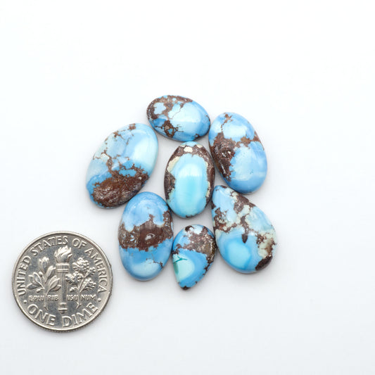 Golden Hills Turquoise cabochons, icy blue to lavender tones with chocolate matrix, polished stones on a white background with a US dime for scale