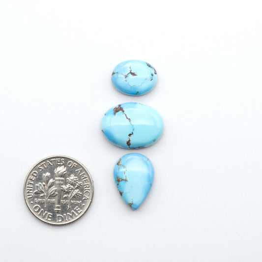 Golden Hills Turquoise cabochons, icy blue to lavender tones with chocolate matrix, polished stones on a white background with a US dime for scale