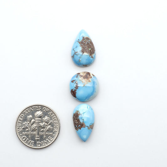 Golden Hills Turquoise cabochons, icy blue to lavender tones with chocolate matrix, polished stones on a white background with a US dime for scale