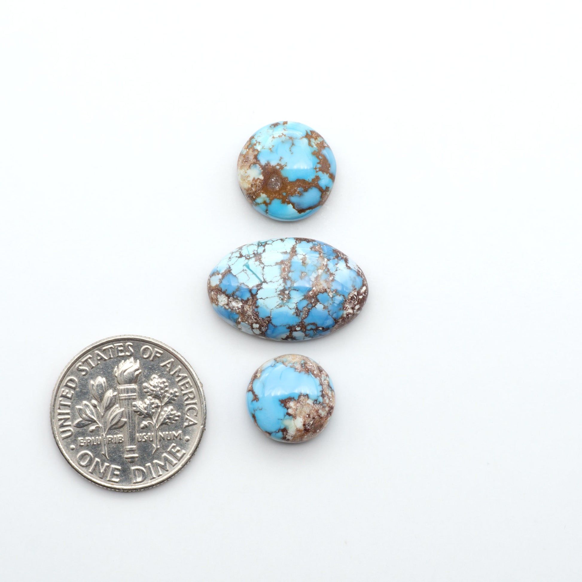 Golden Hills Turquoise cabochons, icy blue to lavender tones with chocolate matrix, polished stones on a white background with a US dime for scale