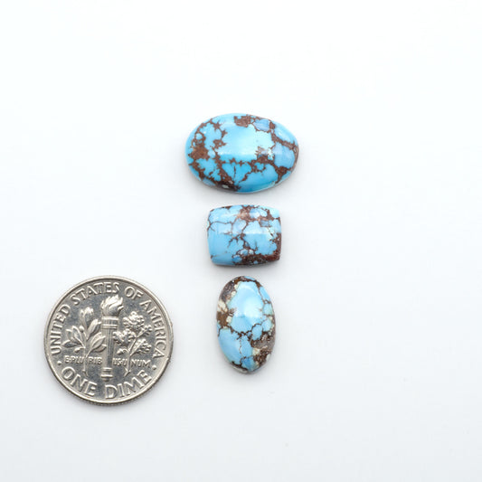 Golden Hills Turquoise cabochons, icy blue to lavender tones with chocolate matrix, polished stones on a white background with a US dime for scale