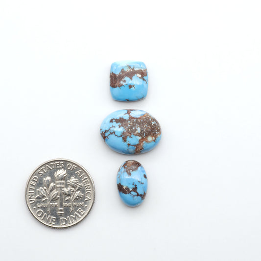 Golden Hills Turquoise cabochons, icy blue to lavender tones with chocolate matrix, polished stones on a white background with a US dime for scale