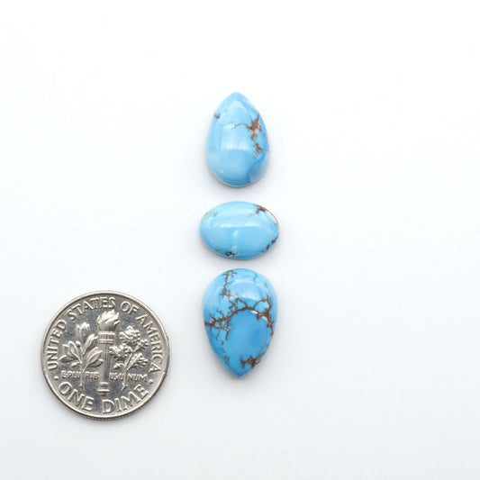 Golden Hills Turquoise cabochons, icy blue to lavender tones with chocolate matrix, polished stones on a white background with a US dime for scale