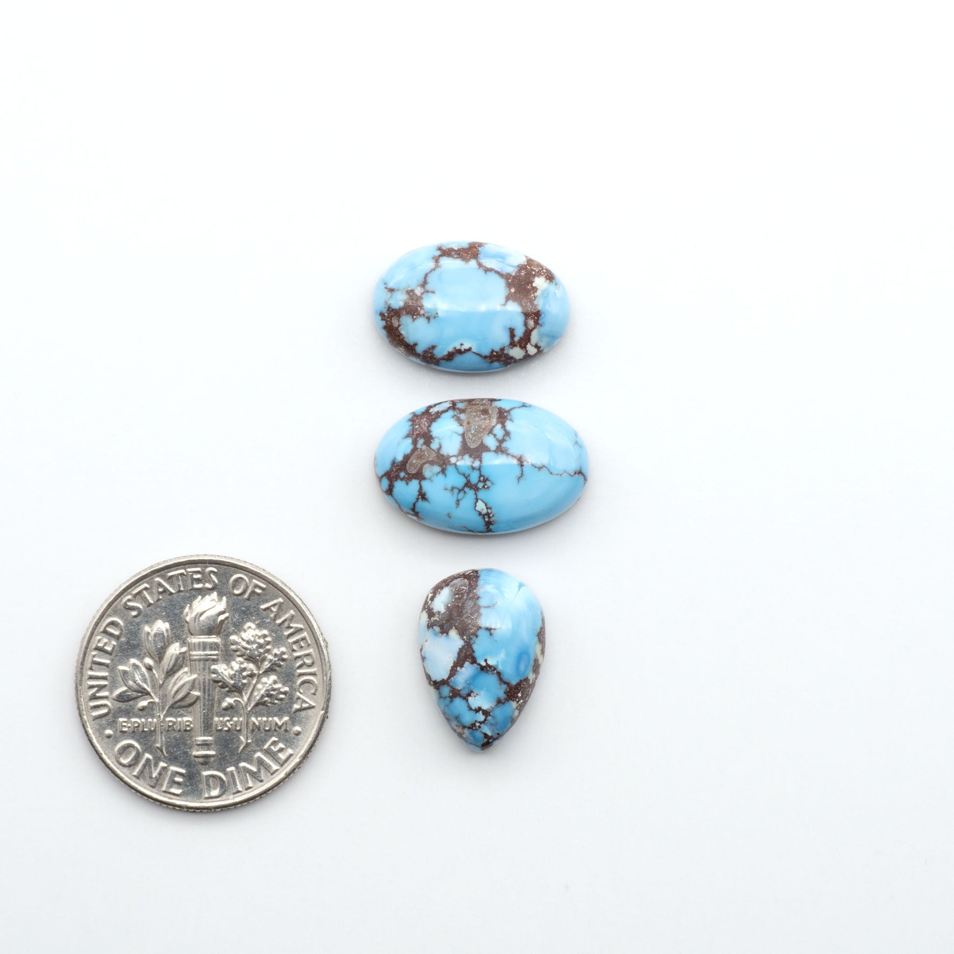 Golden Hills Turquoise cabochons, icy blue to lavender tones with chocolate matrix, polished stones on a white background with a US dime for scale
