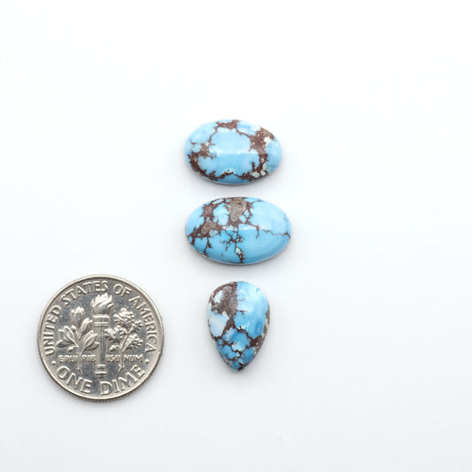 Golden Hills Turquoise cabochons, icy blue to lavender tones with chocolate matrix, polished stones on a white background with a US dime for scale