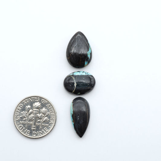 Black Jack turquoise cabochons, blue-green color with black matrix, polished stones on a white background with a US dime for scale