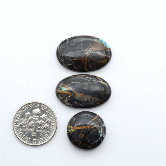 Black Jack turquoise cabochons, blue-green color with black matrix, polished stones on a white background with a US dime for scale