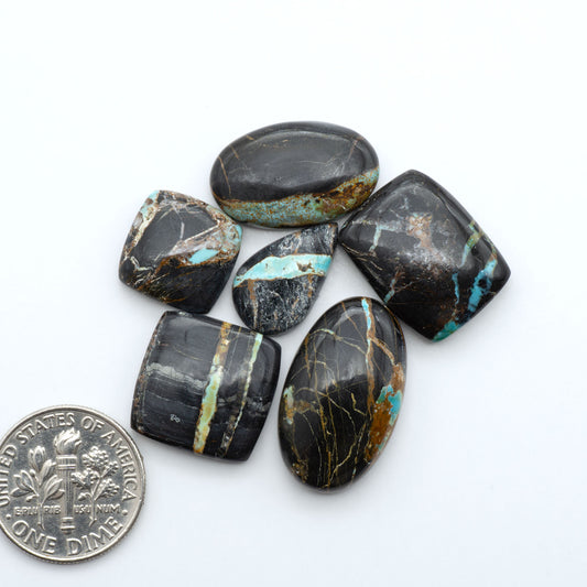 Black Jack turquoise cabochons, blue-green color with black matrix, polished stones on a white background with a US dime for scale