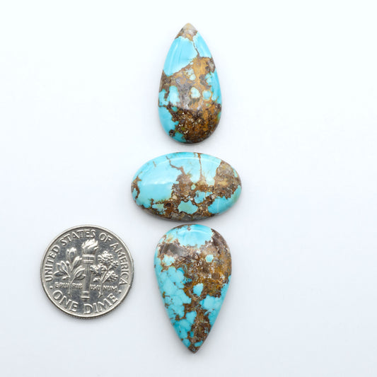 Black Jack turquoise cabochons, blue-green color with black matrix, polished stones on a white background with a US dime for scale