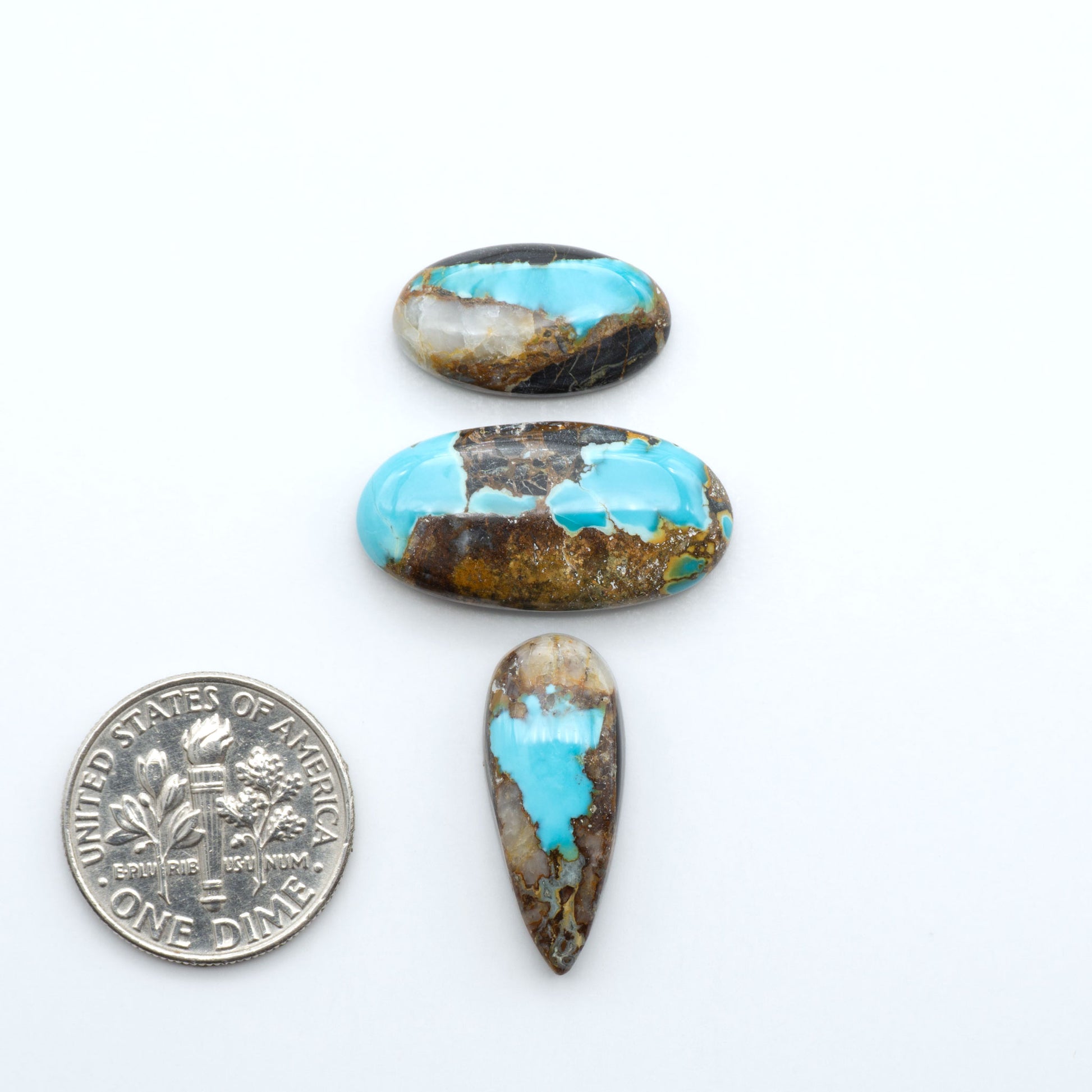 Black Jack turquoise cabochons, blue-green color with black matrix, polished stones on a white background with a US dime for scale