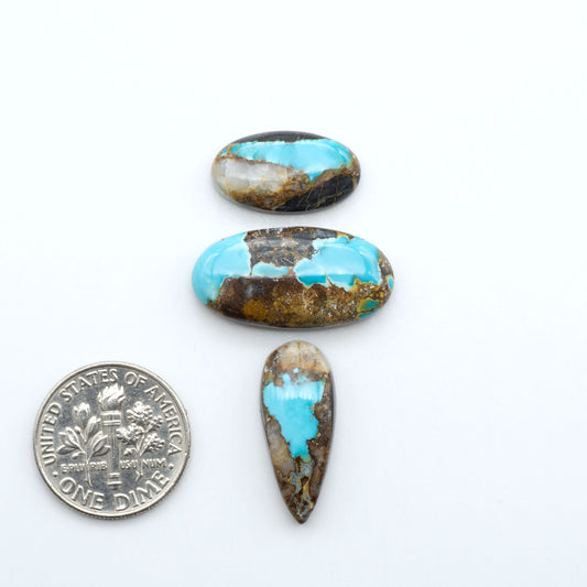 Black Jack turquoise cabochons, blue-green color with black matrix, polished stones on a white background with a US dime for scale