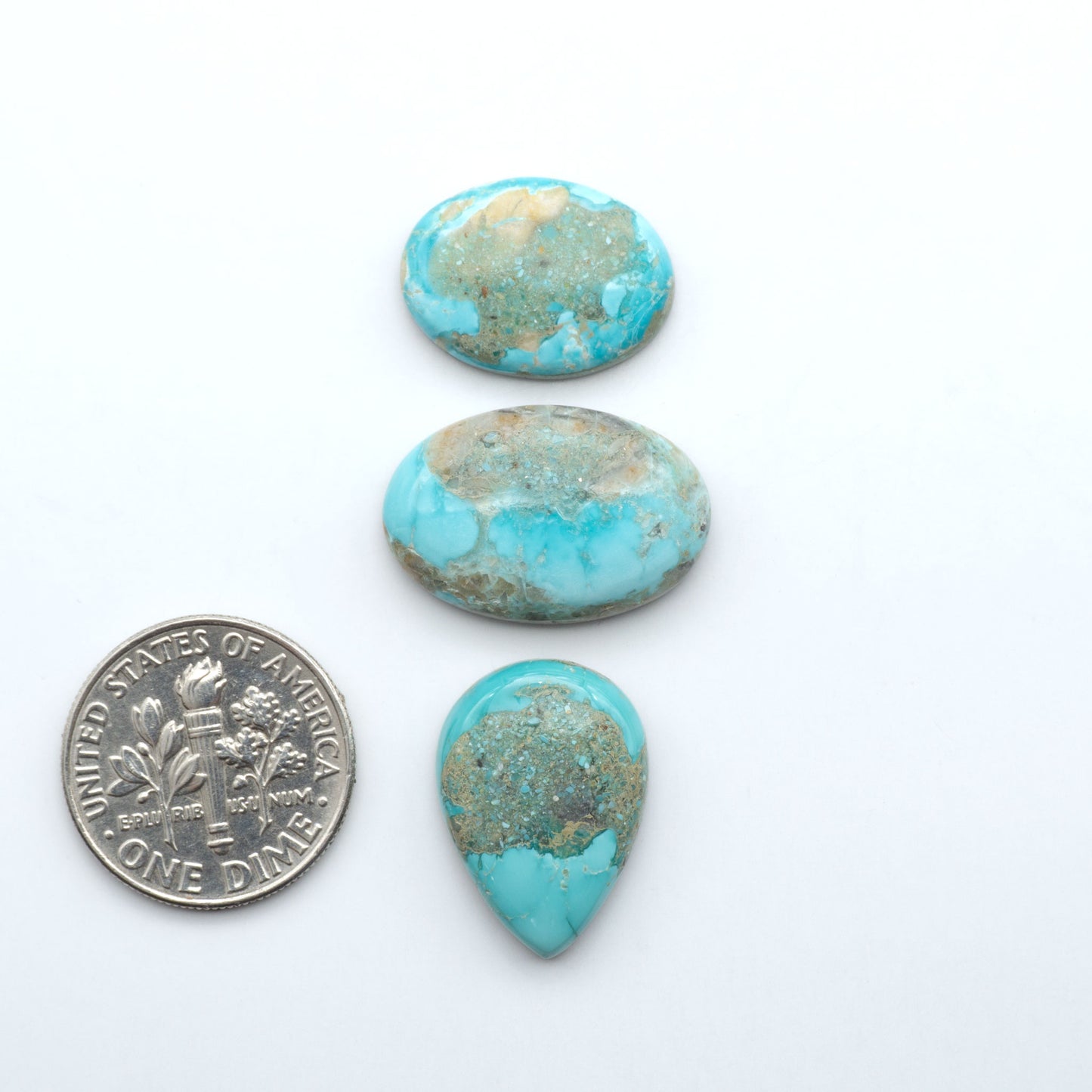 Fox Turquoise cabochons, polished gemstones with natural matrix on a white background, with a US dime for scale