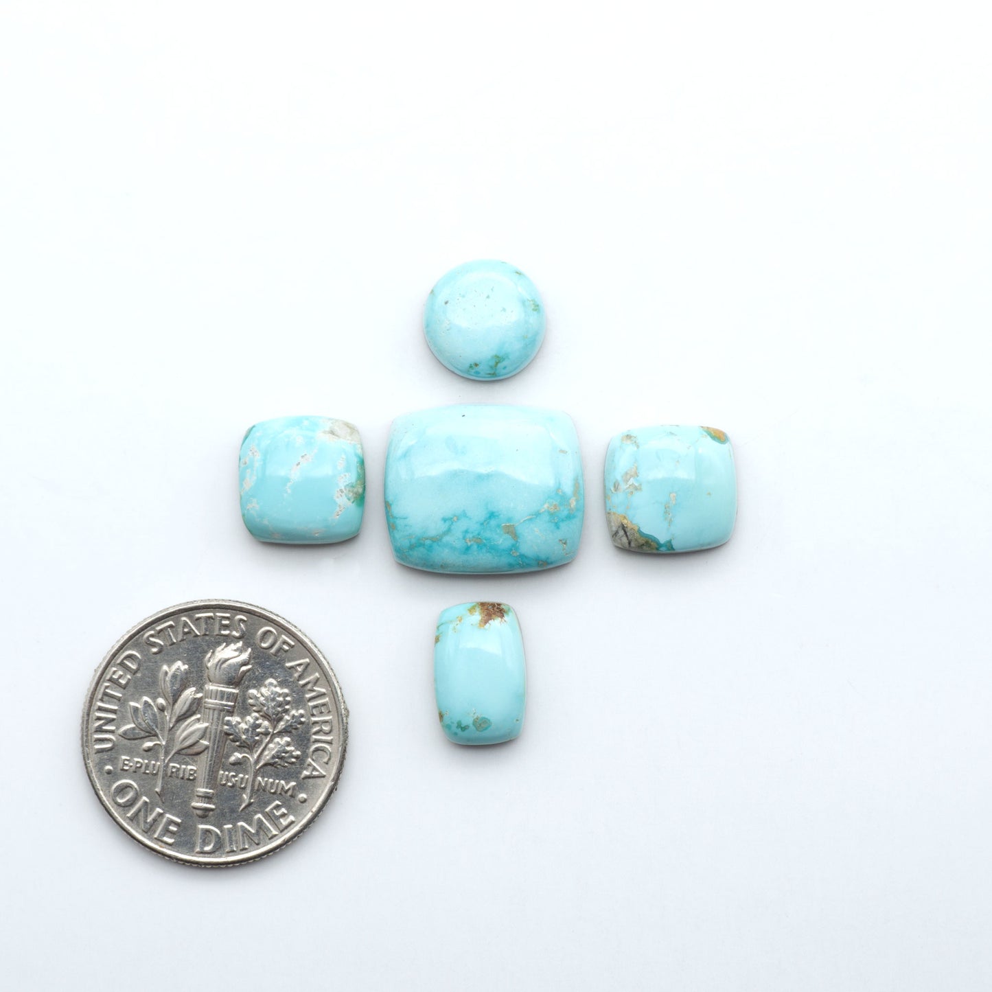 Fox Turquoise cabochons, polished gemstones with natural matrix on a white background, with a US dime for scale