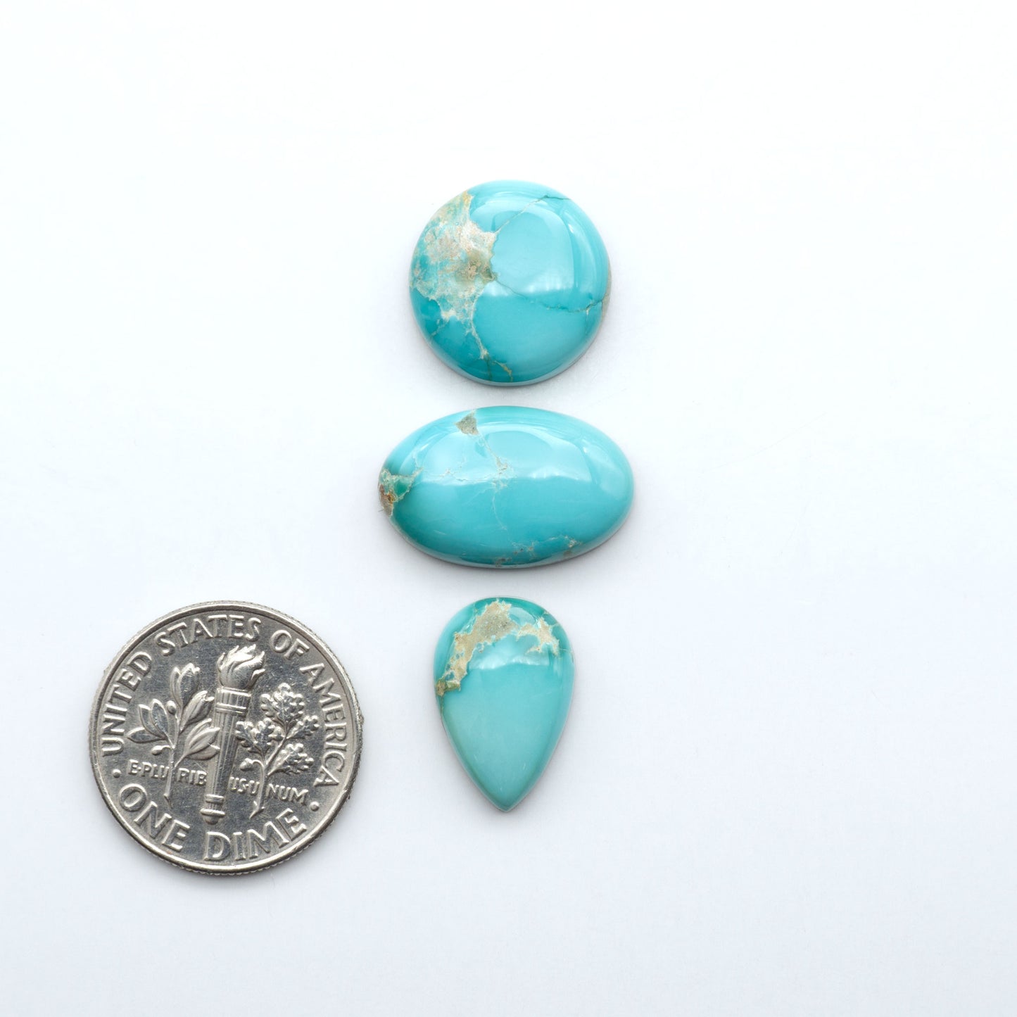 Fox Turquoise cabochons, polished gemstones with natural matrix on a white background, with a US dime for scale