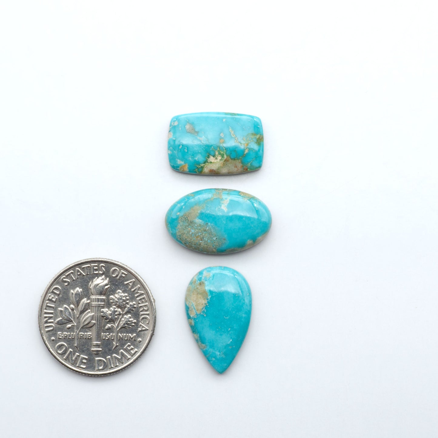 Fox Turquoise cabochons, polished gemstones with natural matrix on a white background, with a US dime for scale
