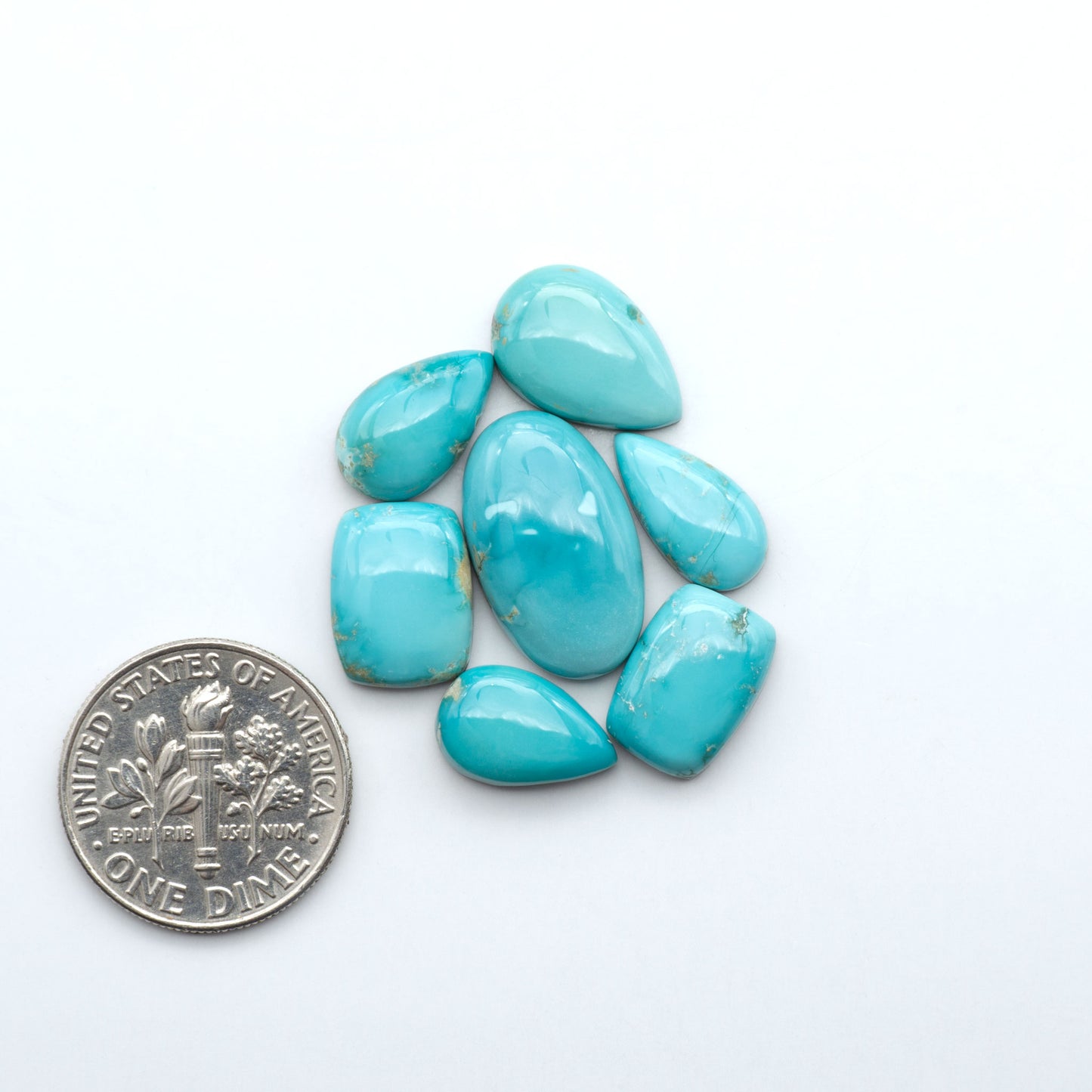 Fox Turquoise cabochons, polished gemstones with natural matrix on a white background, with a US dime for scale