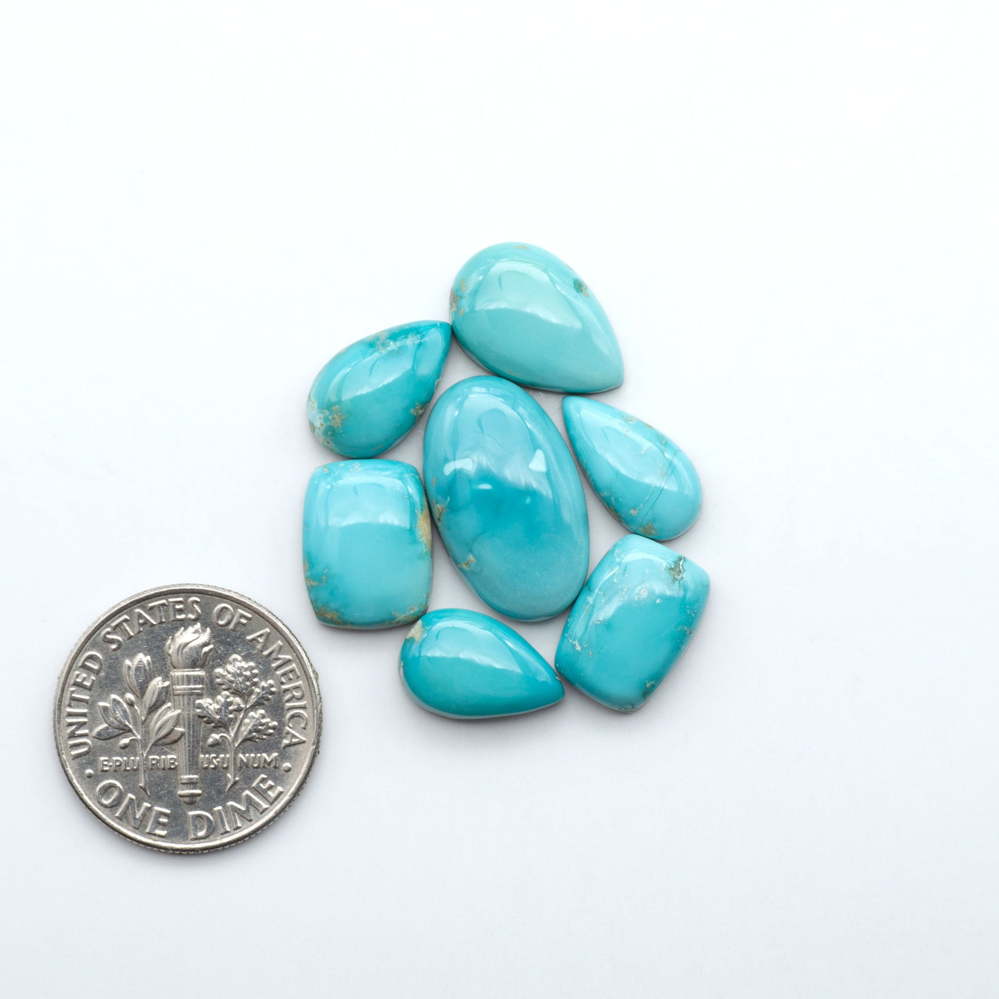 Fox Turquoise cabochons, polished gemstones with natural matrix on a white background, with a US dime for scale