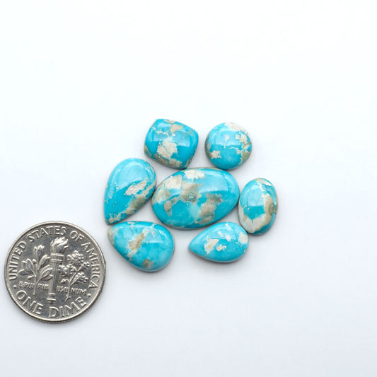 Fox Turquoise cabochons, polished gemstones with natural matrix on a white background, with a US dime for scale