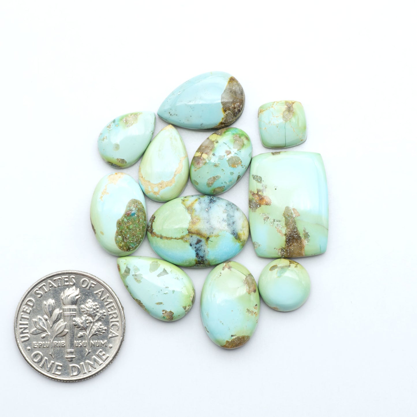 Sonoran Mountain Turquoise cabochons, blue-green color with natural matrix, polished stones on a white background, with a US dime for scale