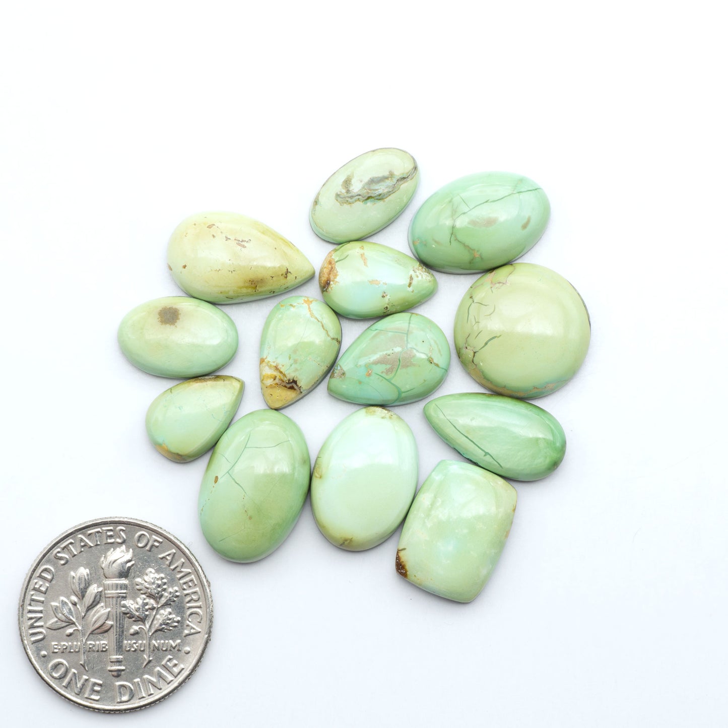 Sonoran Mountain Turquoise cabochons, blue-green color with natural matrix, polished stones on a white background, with a US dime for scale