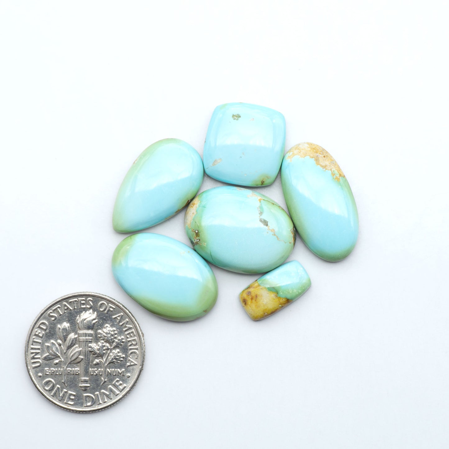 Sonoran Mountain Turquoise cabochons, blue-green color with natural matrix, polished stones on a white background, with a US dime for scale