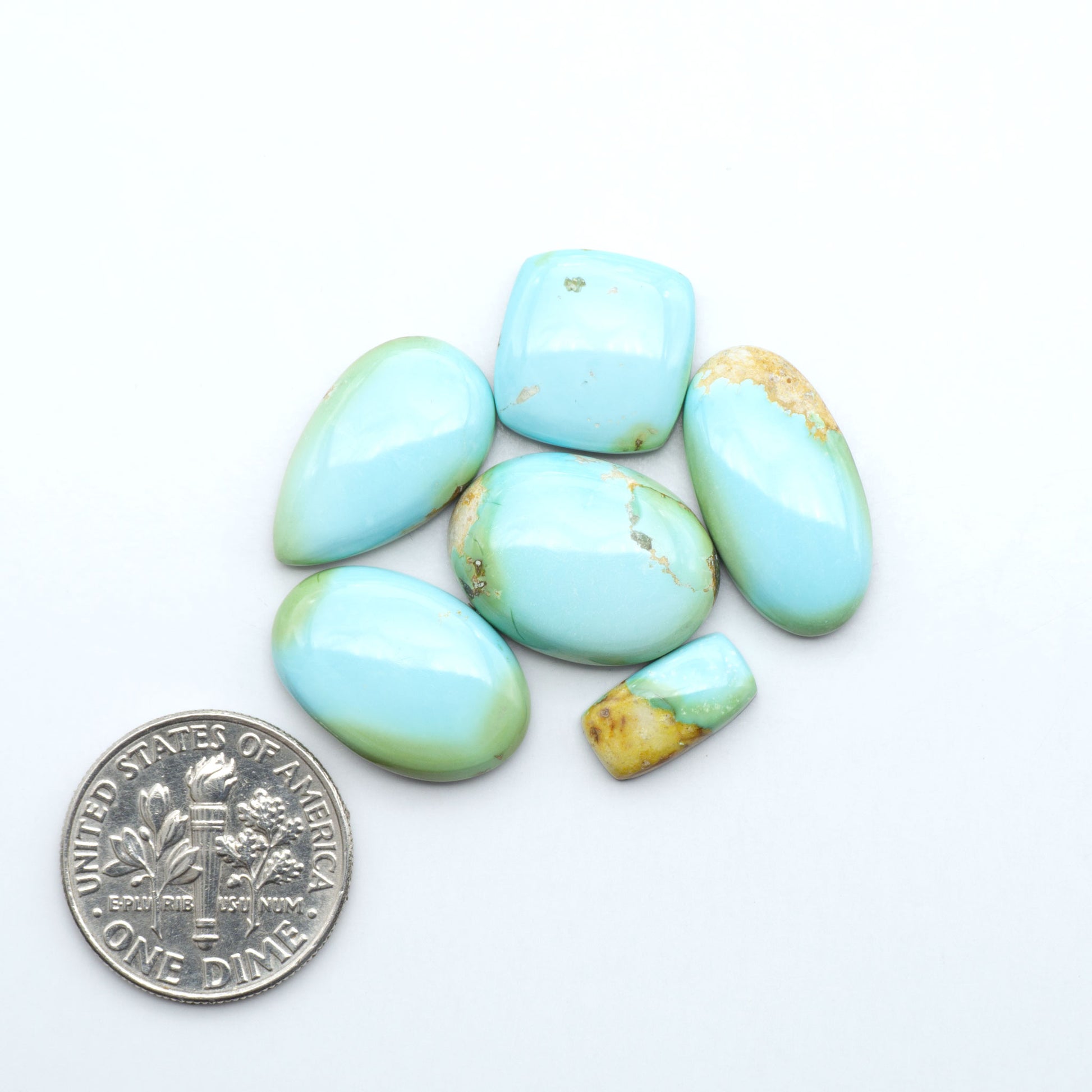 Sonoran Mountain Turquoise cabochons, blue-green color with natural matrix, polished stones on a white background, with a US dime for scale