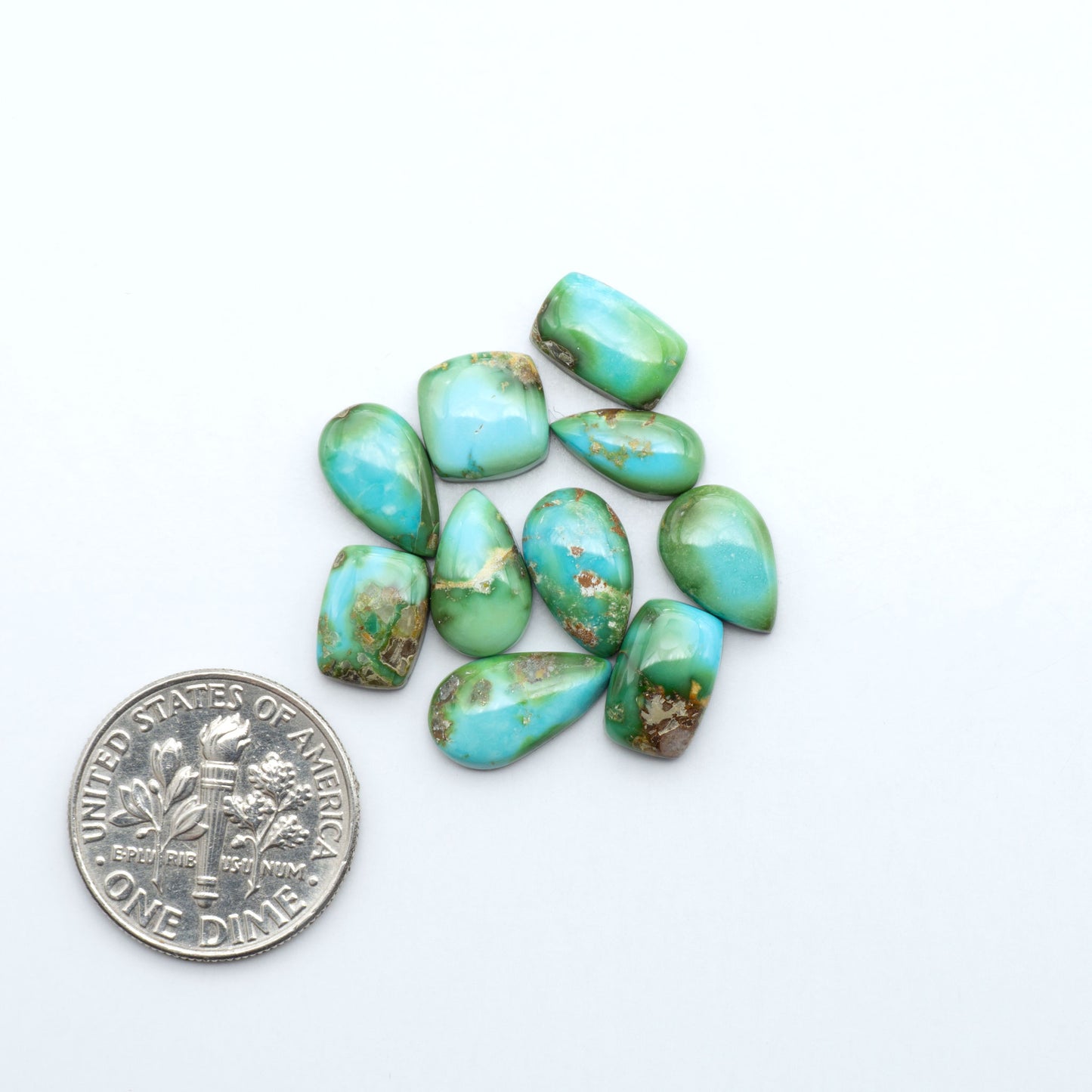 Sonoran Mountain Turquoise cabochons, blue-green color with natural matrix, polished stones on a white background, with a US dime for scale