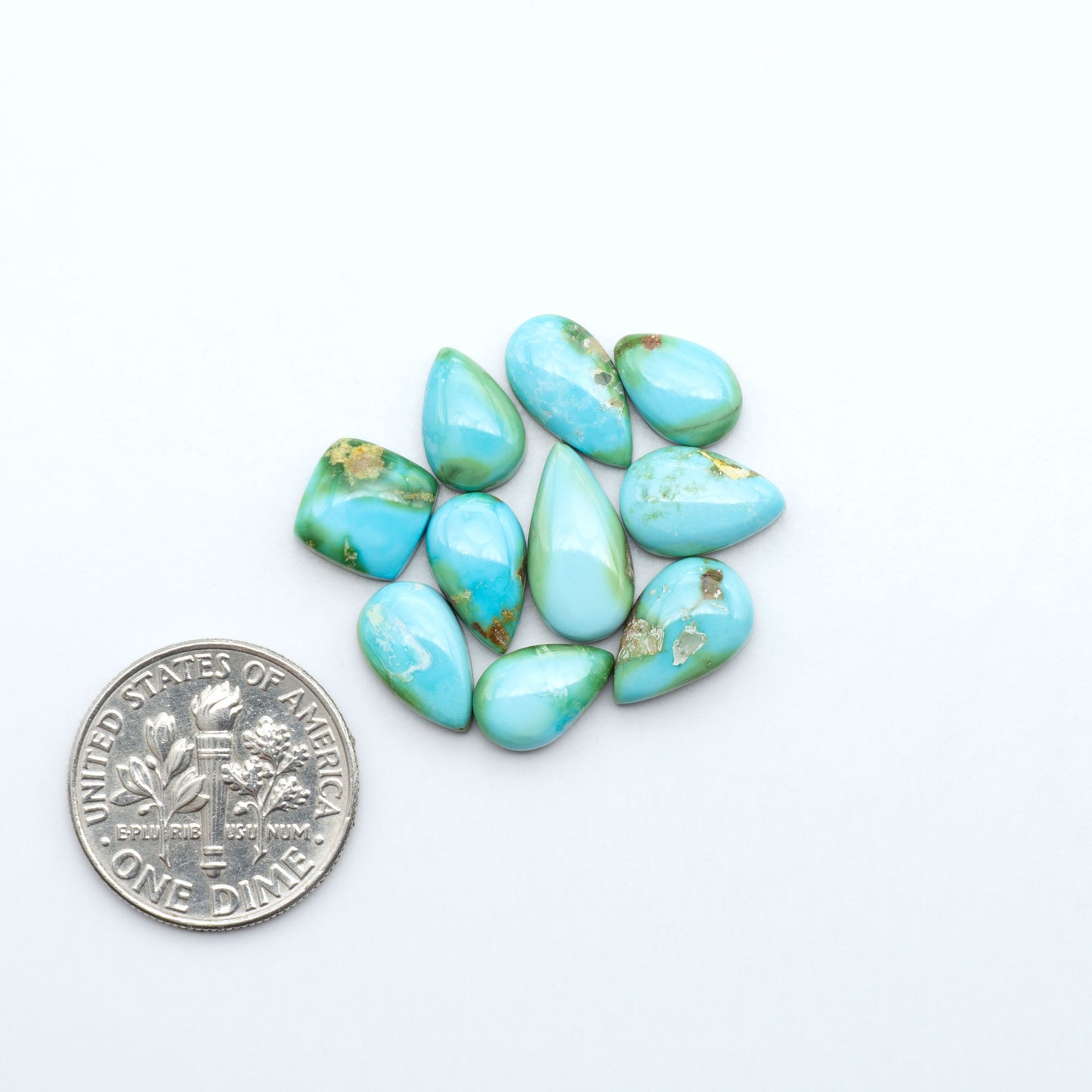 Sonoran Mountain Turquoise cabochons, blue-green color with natural matrix, polished stones on a white background, with a US dime for scale