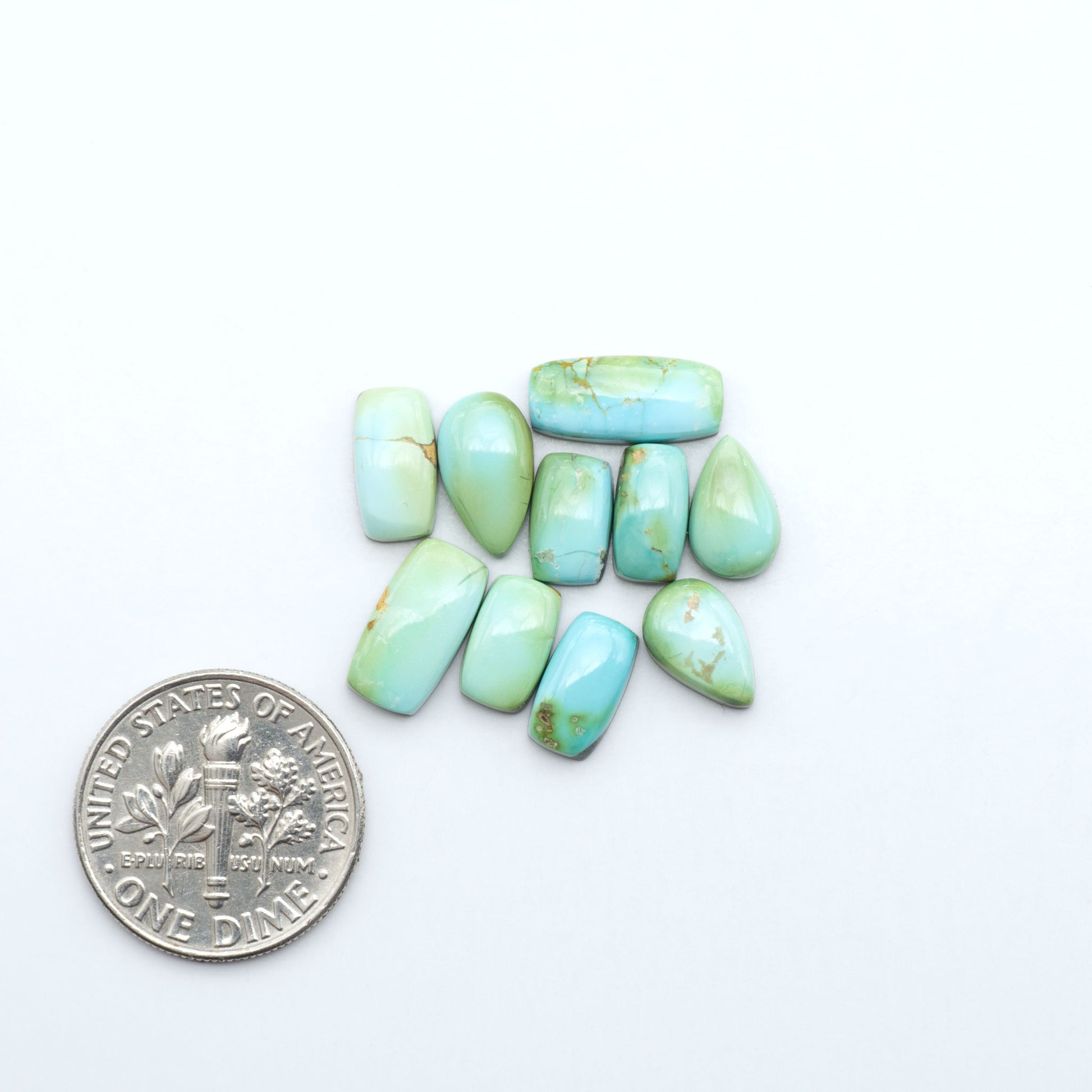 Sonoran Mountain Turquoise cabochons, blue-green color with natural matrix, polished stones on a white background, with a US dime for scale