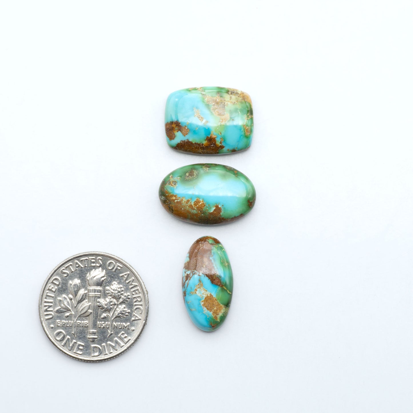 Sonoran Mountain Turquoise cabochons, blue-green color with natural matrix, polished stones on a white background, with a US dime for scale