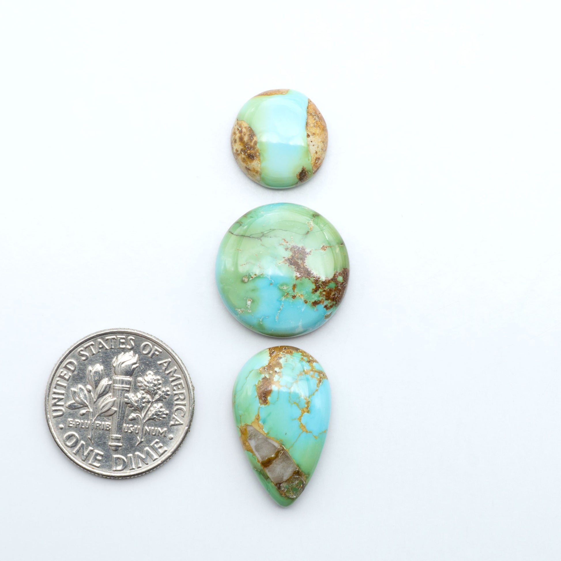 Sonoran Mountain Turquoise cabochons, blue-green color with natural matrix, polished stones on a white background, with a US dime for scale