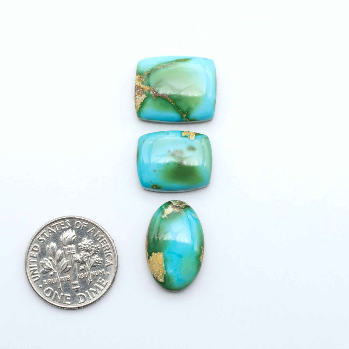 Sonoran Mountain Turquoise cabochons, blue-green color with natural matrix, polished stones on a white background, with a US dime for scale