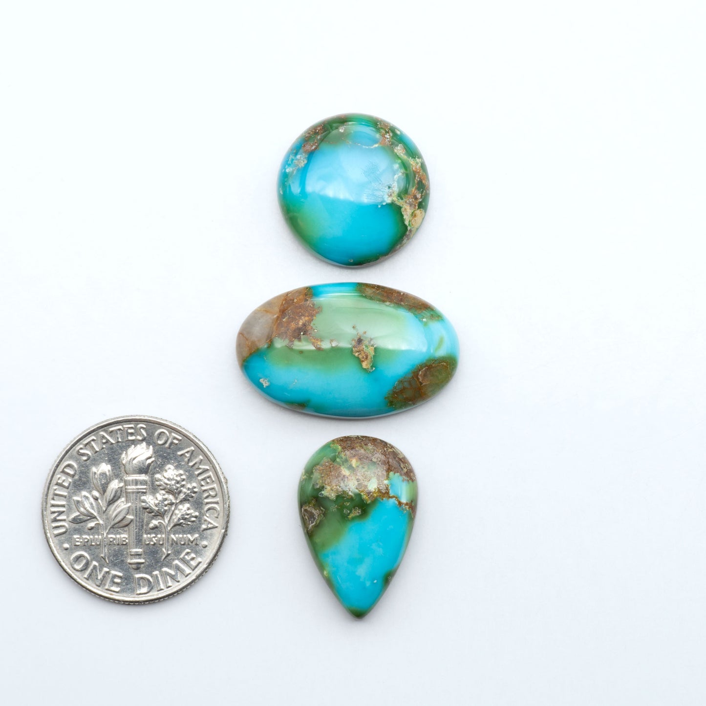 Sonoran Mountain Turquoise cabochons, blue-green color with natural matrix, polished stones on a white background, with a US dime for scale