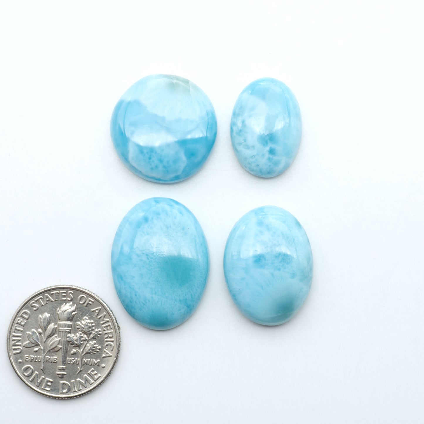 Larimar stone cabochons, cut and polished, blue and white gemstones on a white background, with a US dime for scale