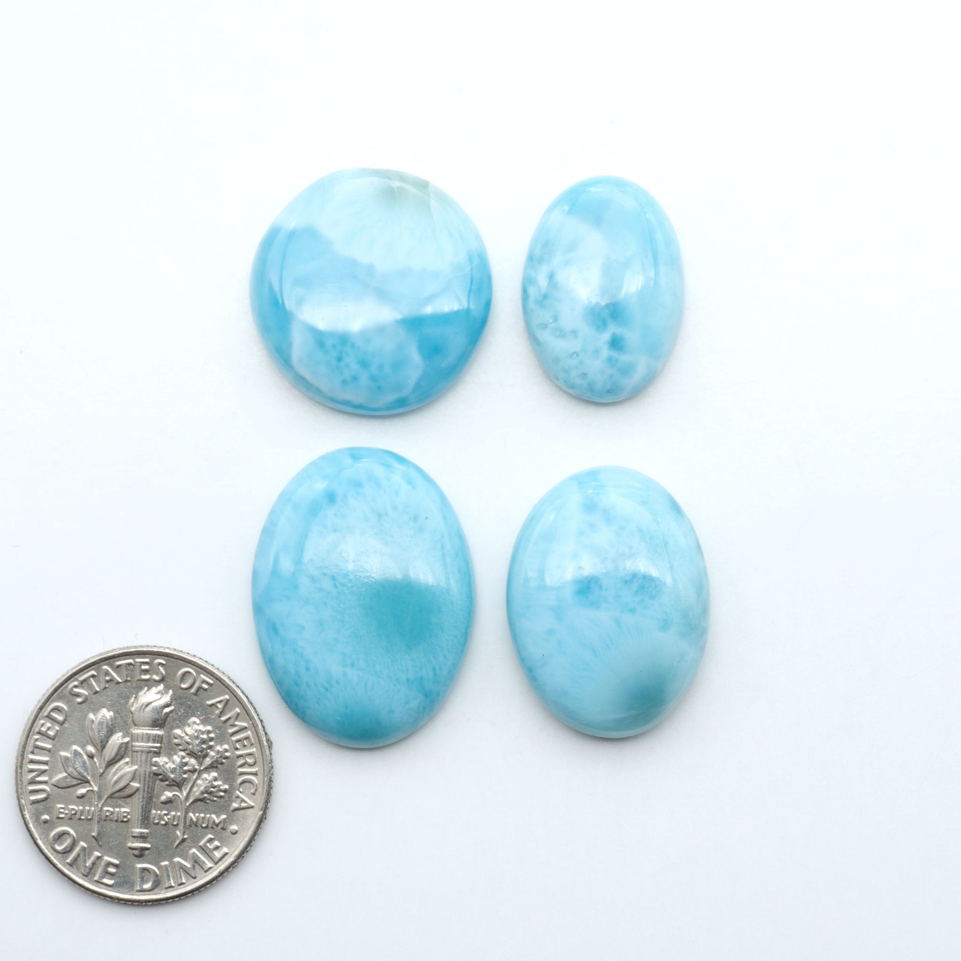 Larimar stone cabochons, cut and polished, blue and white gemstones on a white background, with a US dime for scale